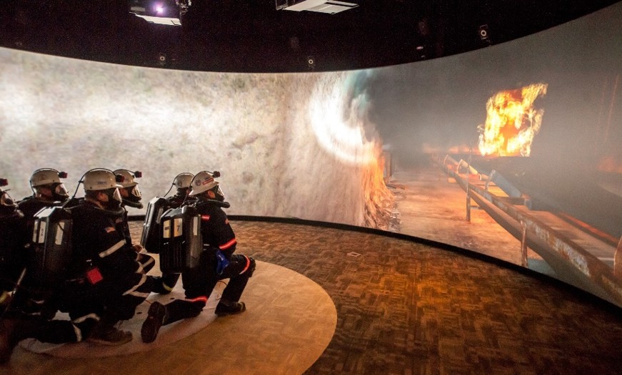 A team of mine rescuers kneeling while looking at a simulated belt fire on the screen in front of them